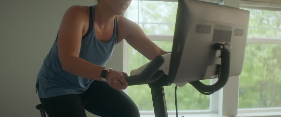 A young woman adjusts her smart exercise bike as she pedals it in her living room during the day