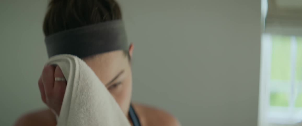 A woman is wiping off sweat from her face as she exercises indoors