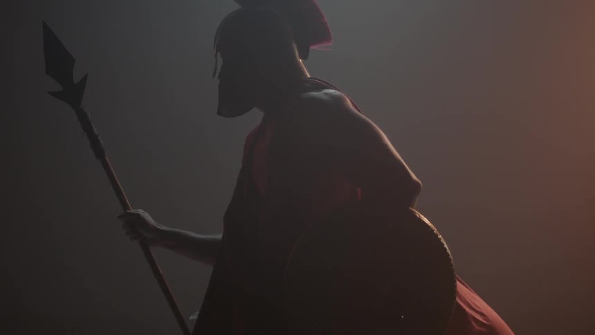 A man is wearing a cape helmet and holding a spear