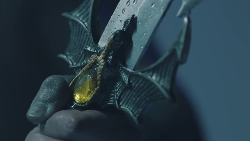 A hand holds the jeweled hilt of a sword