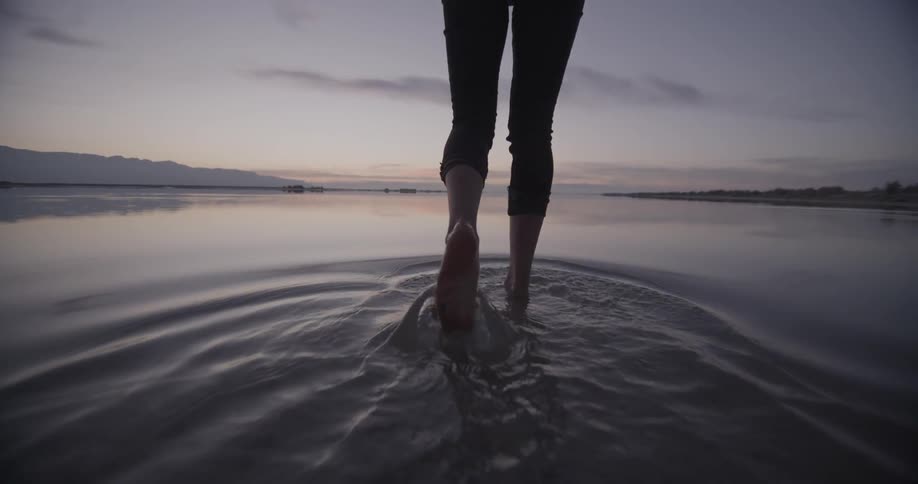 A woman walks into the lake water at sunset