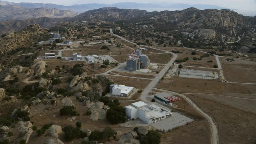 Aerial footage of the Rocketdyne aerospace testing facility in Brandeis California captured during daytime in summer as the camera orbits and flies over buildings surrounded by cloudy skies