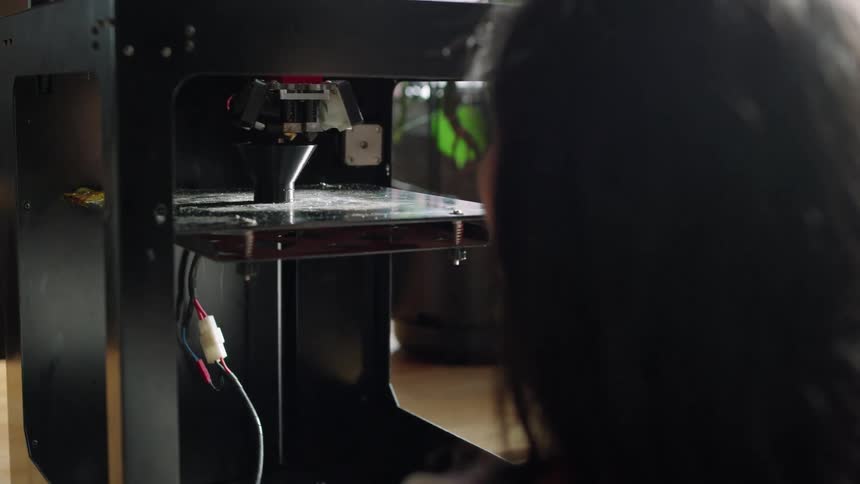 A woman is watching as a three dimensional printer is creating an object