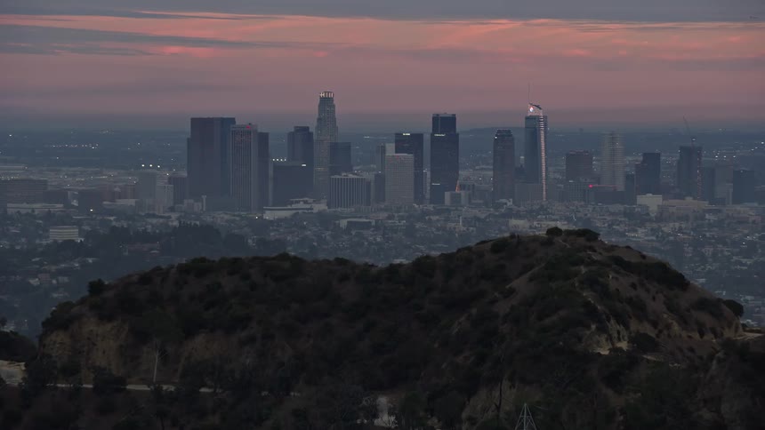 A breathtaking aerial shot of Downtown Los Angeles at twilight showing towering skyscrapers and high rises from behind a hill in California