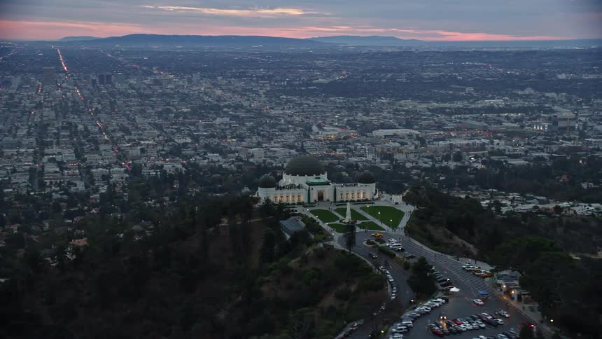 Aerial footage of the iconic Griffith Observatory orbiting to reveal the city skyline and sprawl during twilight in Los Angeles California