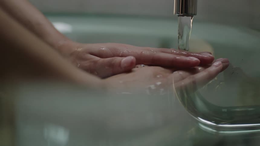 A faucet pours water over a person's hands