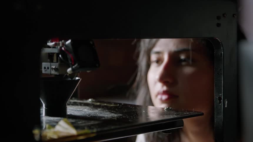 A woman observes closely as a 3d printer creates a small object
