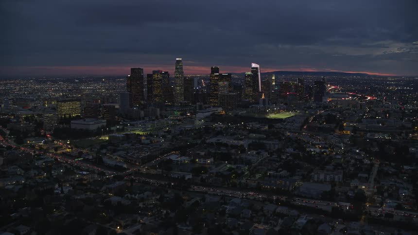 Stunning aerial footage of Downtown Los Angeles at twilight captured from a height of over the 101 freeway during summer showcasing high rise towers superstructures and skyscrapers with a beautiful skyline and partly cloudy skies