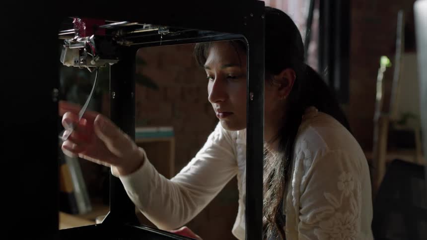Young long haired woman extracts the plastic filament from a 3d printer in the office