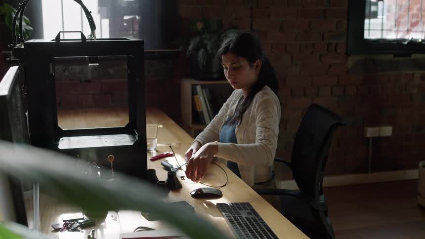 A woman sitting at her desk taking apart equipment setting it down and looking at it
