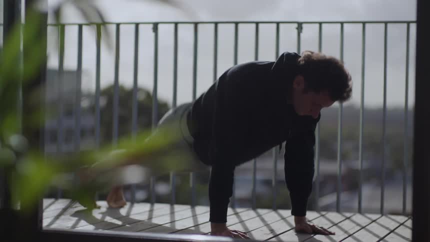 A man is stretching outdoors on his balcony