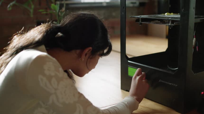 A woman is operating a three dimensional printer as it is creating an object