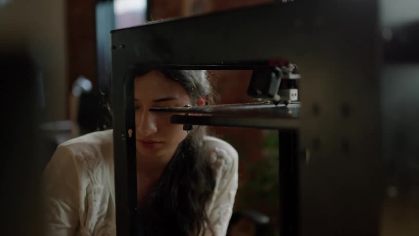 A woman looks closely as she compares the object shes holding to one being 3d printed