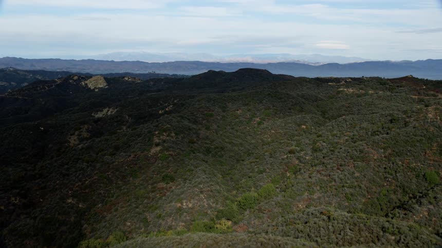 Flying over the Santa Monica Mountains in California on a cloudy day approaching and flying over the hills and valleys in Malibu during summer