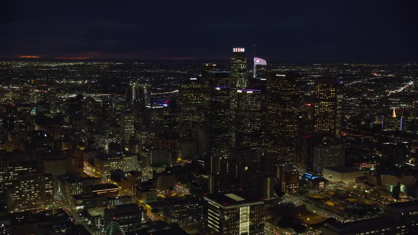 Fly over downtown Los Angeles towering skyscrapers at night during the warm summer months in epic Helium-shot footage