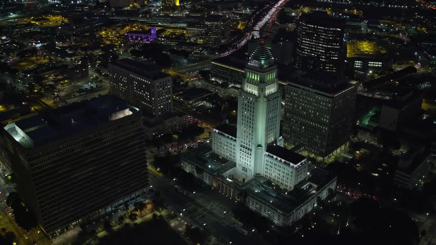 Night aerial view of Downtown LAs skyscrapers revealing the illuminated City Hall building in the center