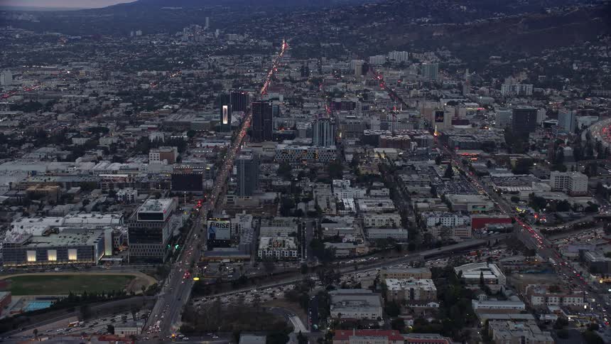 Approaching Sunset Boulevard and its neighboring businesses during twilight in Hollywood California as seen from an aerial view