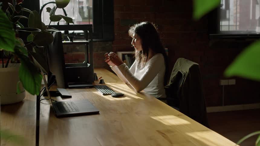 A woman sitting at a desk in an office using a 3d printer to fabricate some things