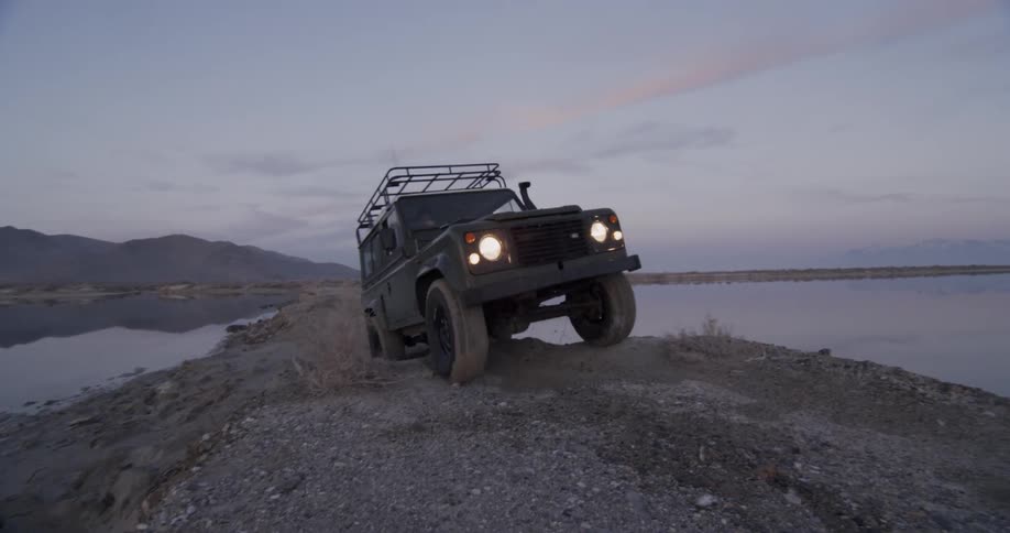 A vehicle is driving over rocks near a lake