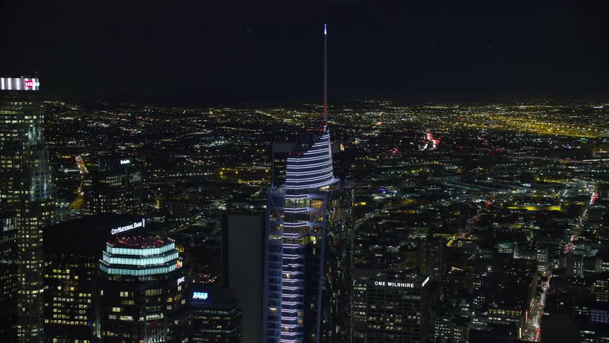 A glittering high rise shot from above as it stands amidst the modern glass buildings of Downtown Los Angeles at night