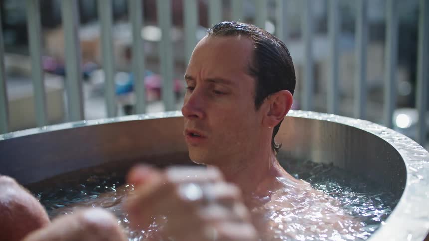 A man reclining in an ice bath quickly dunks his head under the water and resurfaces