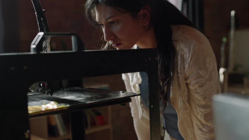 Woman leans down to examine active arm of 3d printer