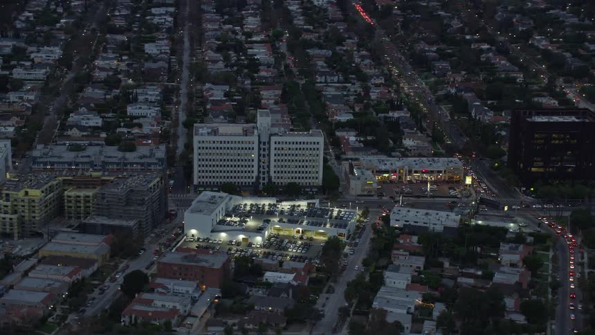A twilight aerial footage of Wilshire La Brea apartments and Consulate General of Spain on Wilshire Boulevard in Central Los Angeles surrounded by office and government buildings residential apartments and partly cloudy skies during summer