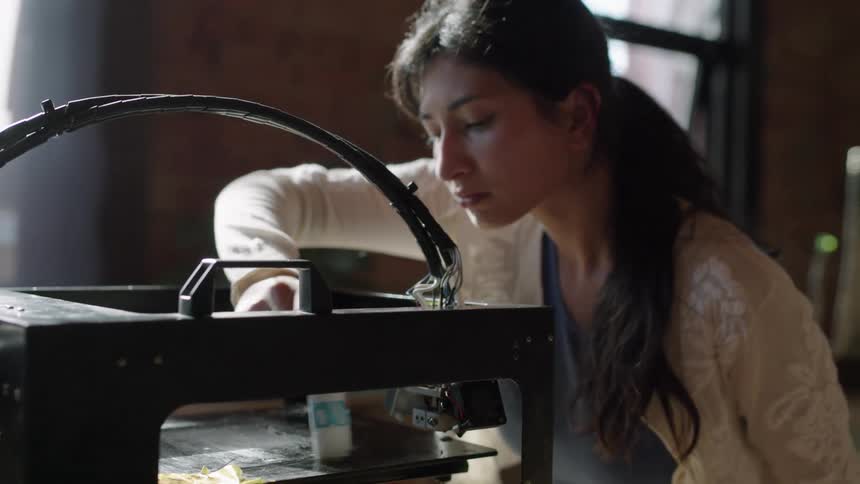 Woman applies paste onto surface in machine while working in brick walled room