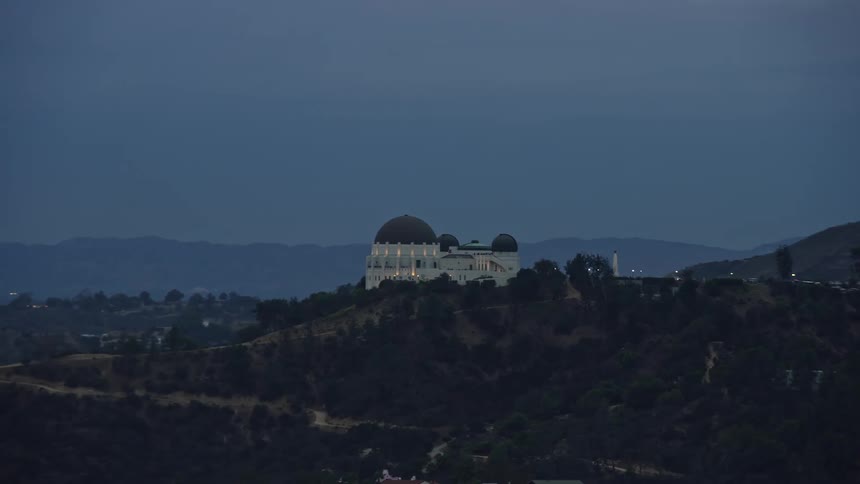 A stunning twilight aerial clip tracking the iconic Griffith Observatory in Los Angeles California before revealing the famous Hollywood Sign in the partly cloudy skies of Southern California during Summer
