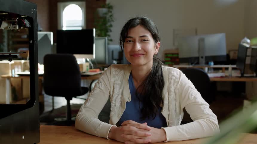 Young happy woman smile at the camera while sitting at a desk in the office