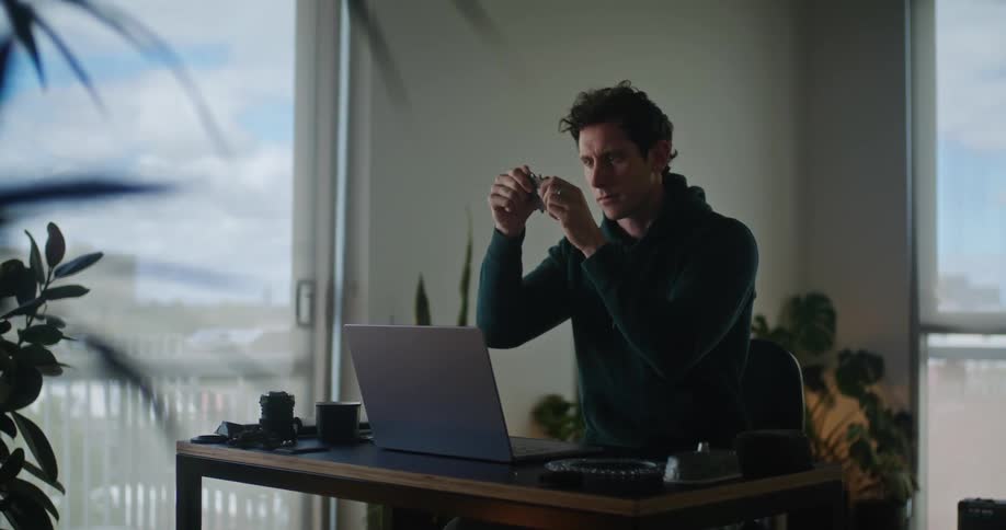 A man is sitting at his computer desk and looking at an object