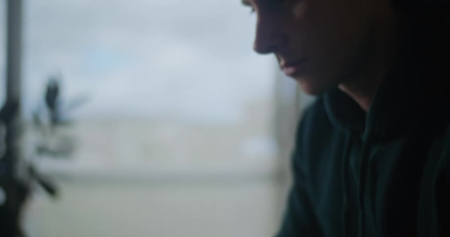 A man is sitting at a desk typing on the keyboard of a laptop computer