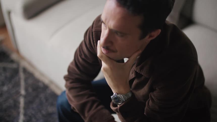 Man with mustache brown shirt and jeans works on laptop in the living room