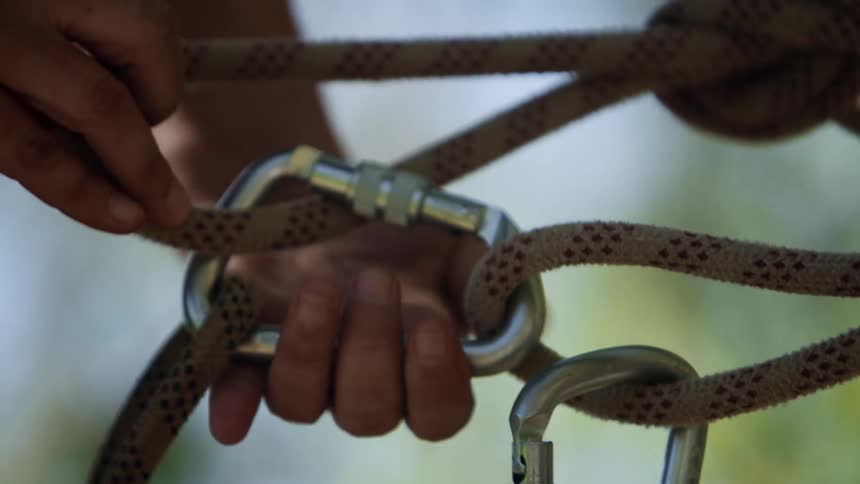 A close up of a persons hand clipping a rope and tightening the clip