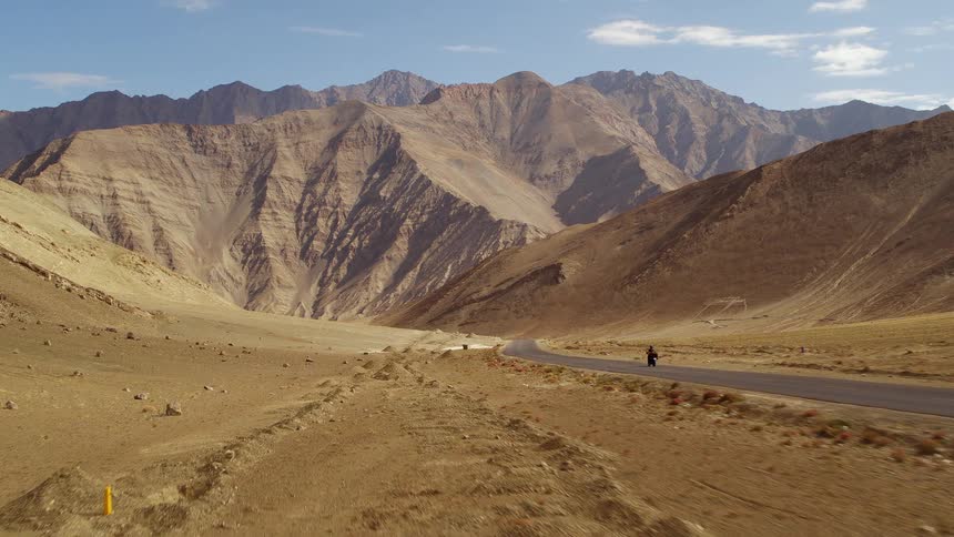 Motorcyclist rides along highway through arid land toward mountains