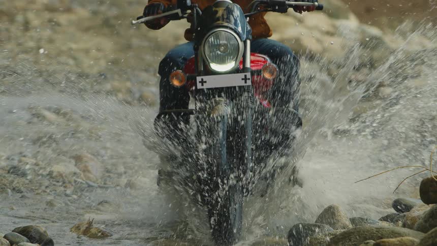 Motorcycle riding across rock creek filled with water