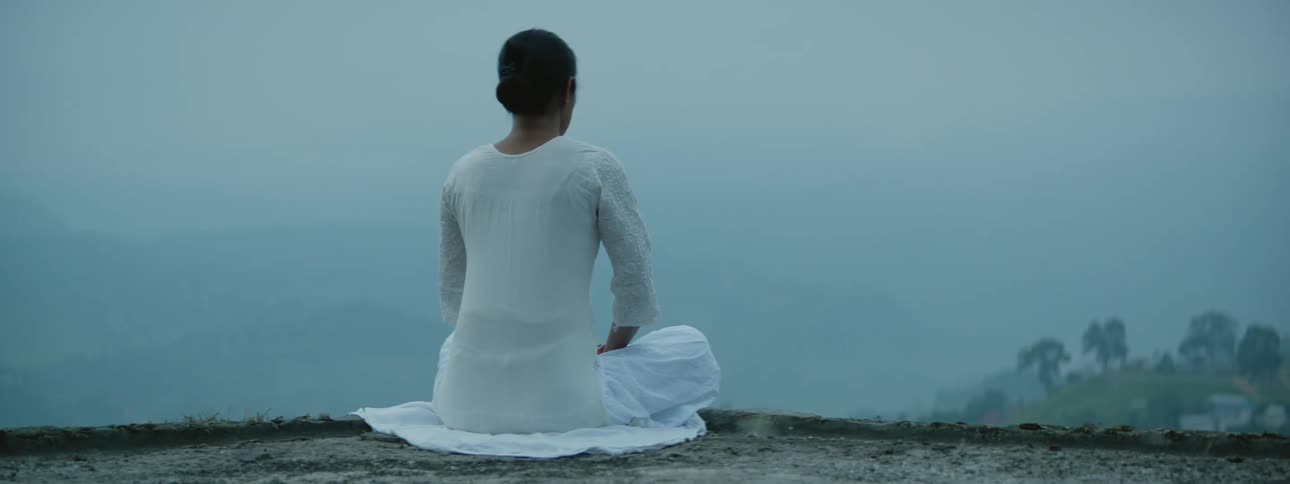 A person sits on the top of the mountain meditating on a foggy day