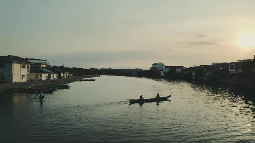 A waterway with a boat on it with two people in it with houses on either side of the waterway
