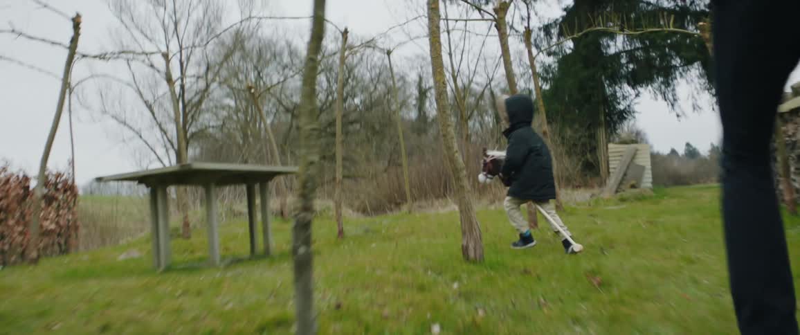 Father chases child across lawn near water as child rides hobby horse