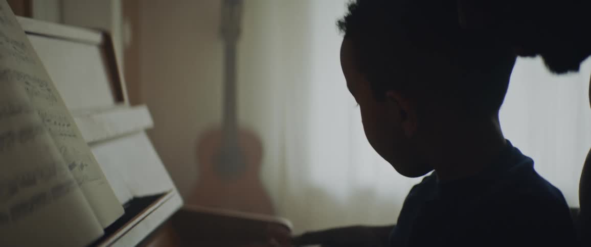 A curious toddler plays with a piano with his father