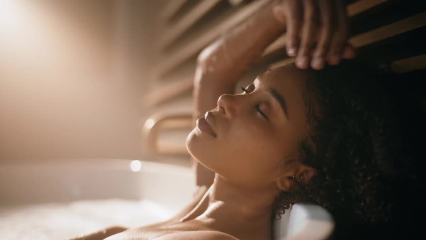 Woman lies in bathtub touching her curly hair