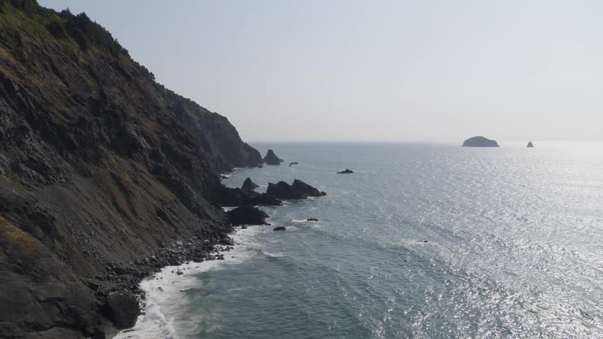 Sparkling ocean waves break along the rocks of a rugged and dramatric coastal mountainside