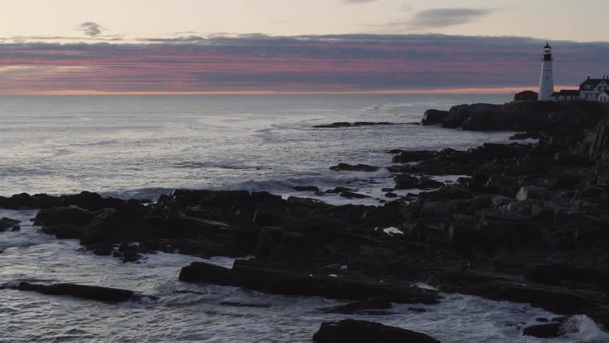 Reveal of a beautiful lighthouse along a rocky shoreline under a painted sky