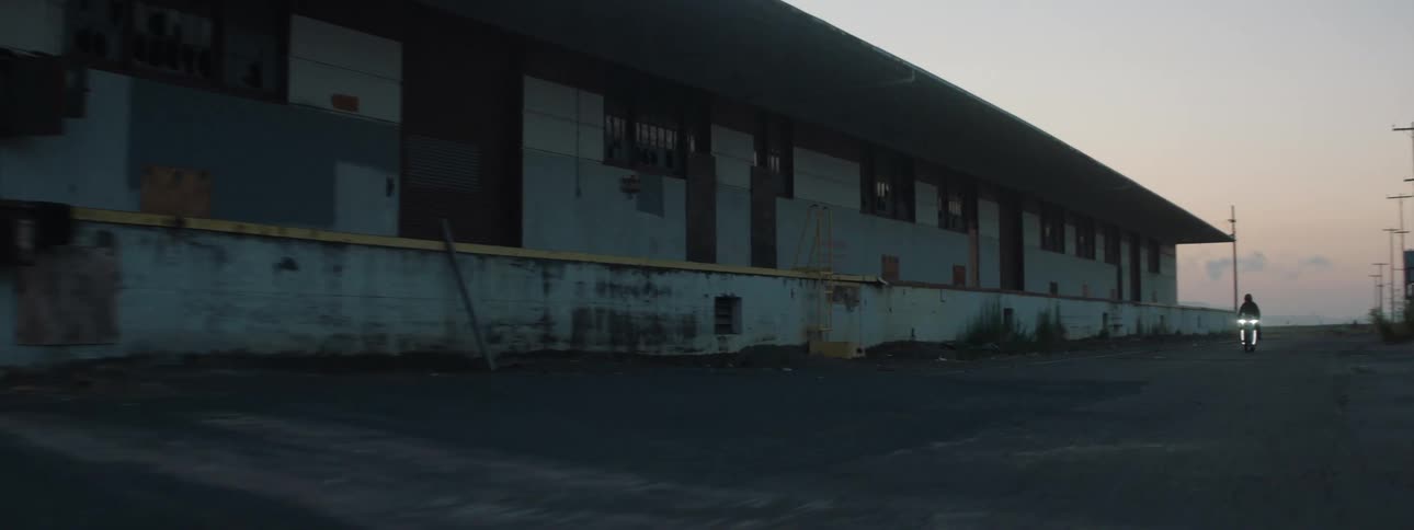 Motorcycle rider driving on asphalt next to a warehouse at dusk