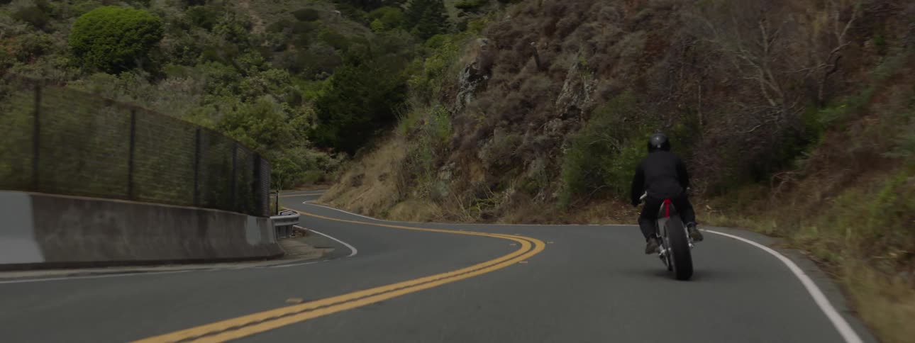 A motorcycle travels on a winding mountain road as the rider is wearing a black jacket and helmet