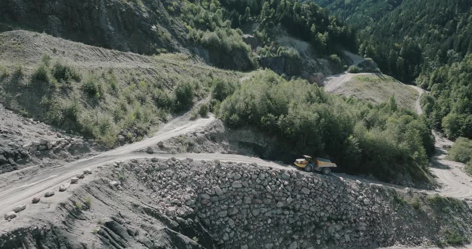 A large dump truck slowly drives up a dirt road as it ascends a hill