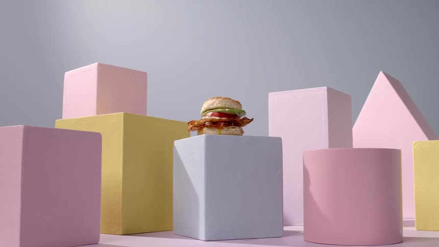 A burger sitting on a square block surrounded by other shapes