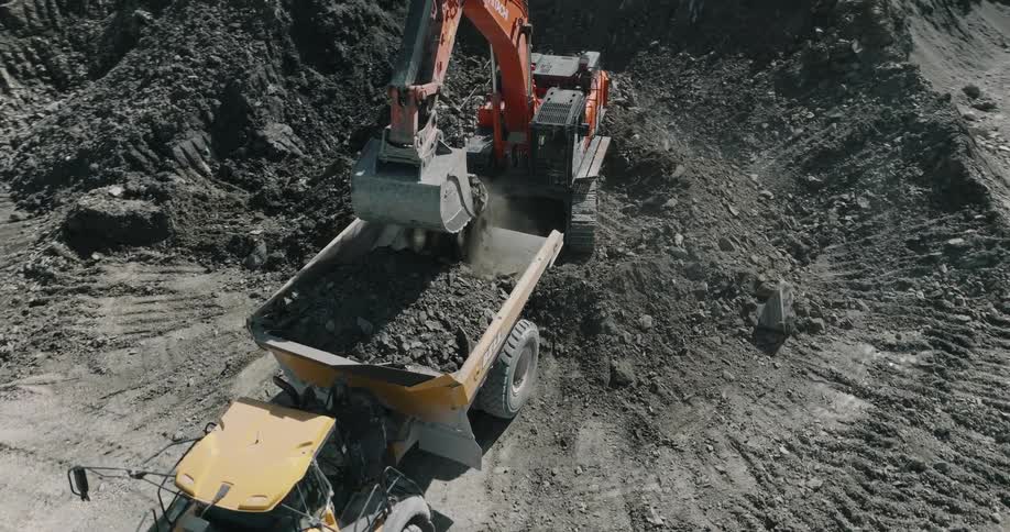 A gravel pit with an orange excavator dumping gravel into a yellow dump truck