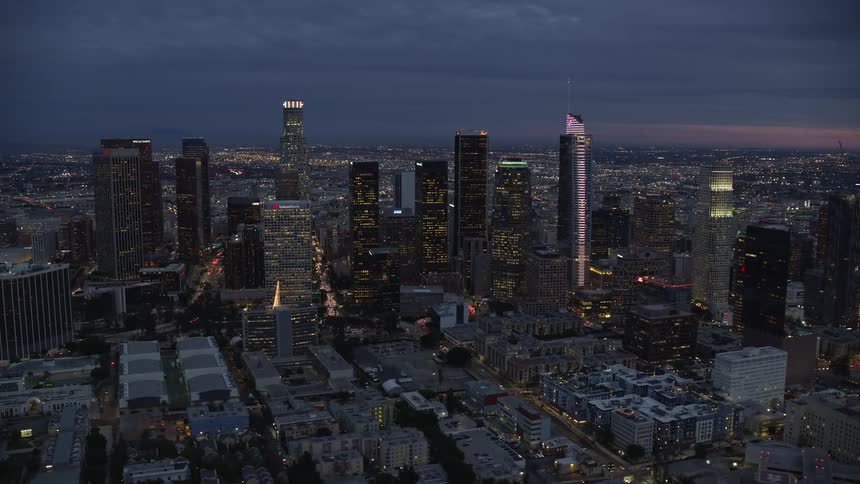 A breathtaking aerial footage at twilight of tall skyscrapers lighting up the heart of Downtown Los Angeles during summer showcasing its highways heavy traffic and entertainment scene shot with Shotover F1 technology