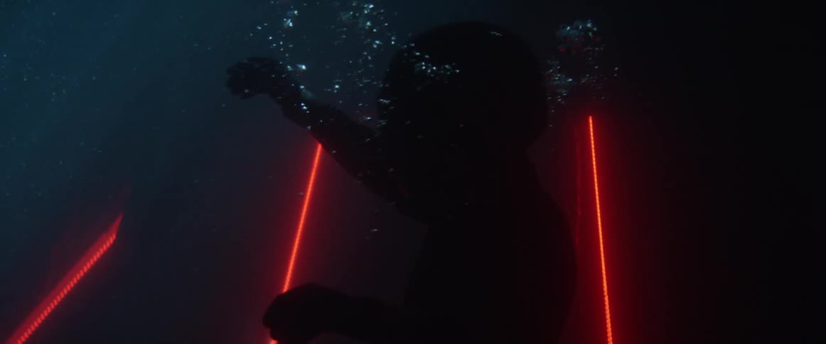 A man wearing a helmet on his head and swimming into deep water with red lights in the water